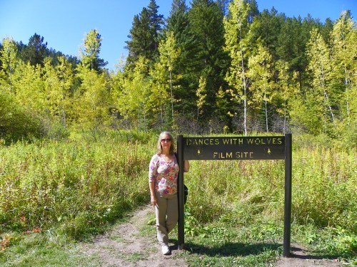 A person stands beside a sign for the "Dances With Wolves" film site, surrounded by trees and greenery.
