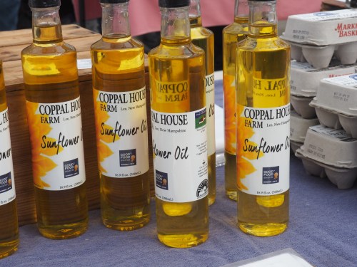 Bottles of sunflower oil labeled "Coppal House Farm" displayed at a market, with eggs in the background.
