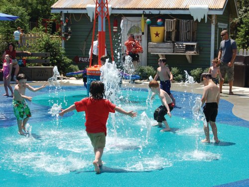 Children playing in a splash pad, joyfully running through water sprays on a sunny day.