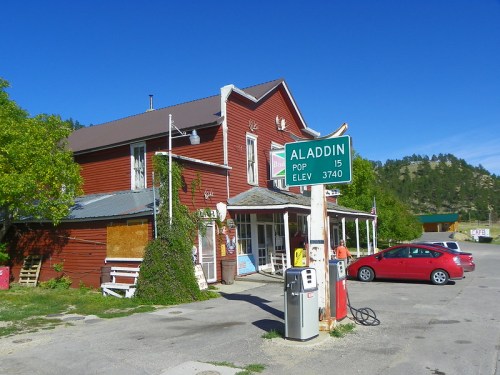 A red building with a sign for Aladdin, population 15, and an elevation of 3,740 feet, set against a clear blue sky.