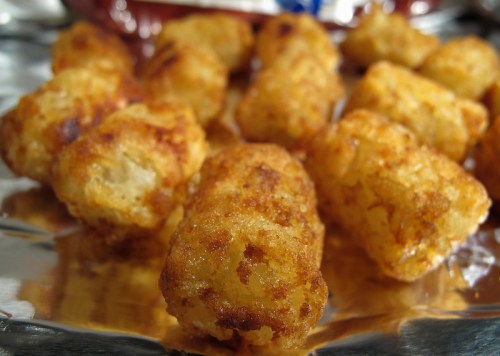 Golden-brown tater tots arranged on a shiny foil surface, showcasing a crispy texture.