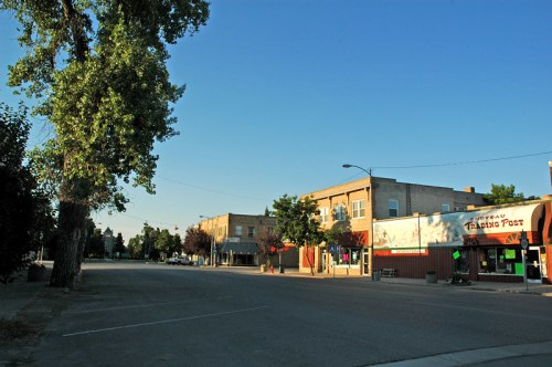 A quiet street scene with trees, buildings, and clear blue sky, showcasing a small town atmosphere.