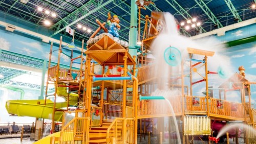 Colorful indoor water park play structure with slides, water features, and a large water bucket tipping over.