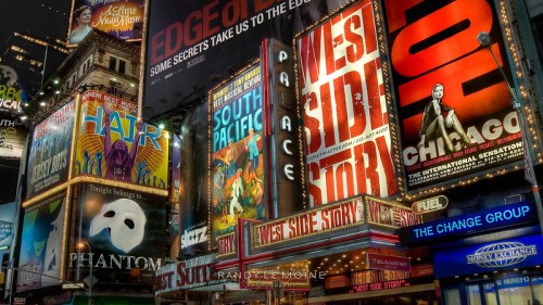 Brightly lit Broadway theater marquee featuring posters for "West Side Story," "Chicago," "Phantom," and more.