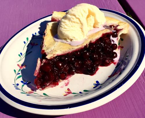 A slice of berry pie topped with a scoop of vanilla ice cream on a decorative plate.