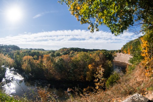 A panoramic view of a river surrounded by colorful autumn foliage under a bright blue sky.