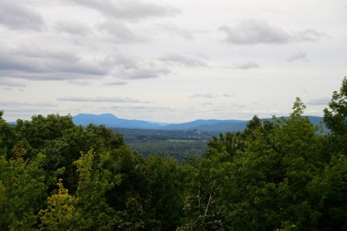 A scenic view of rolling mountains and lush green trees under a cloudy sky.