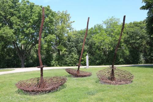 Three large, abstract sculptures resembling baskets or boats, made of twisted metal, set in a grassy area with trees.