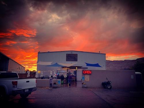 A building with an "OPEN" sign under a vibrant sunset sky, with people outside and a motorcycle parked nearby.