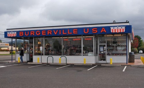 A fast-food restaurant named Burgerville USA with a red, white, and blue sign, featuring a modern glass facade.
