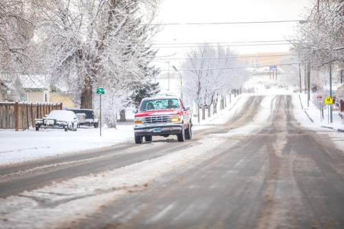 A red truck drives down a snowy street lined with frosted trees and power lines.
