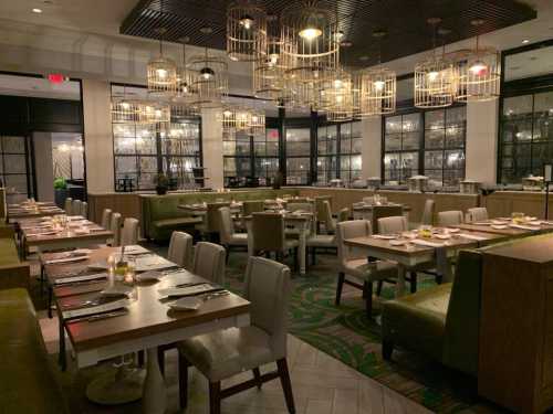 A modern restaurant interior featuring green seating, wooden tables, and stylish hanging light fixtures.