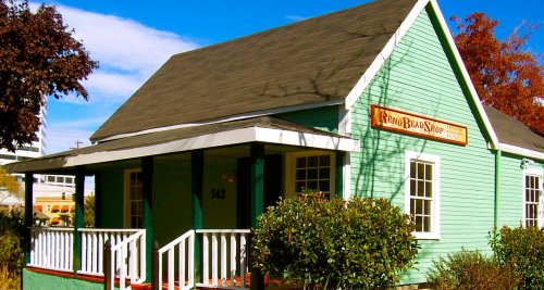 A green house with white trim and a sign reading "Reno Bean Shop" surrounded by trees and shrubs.