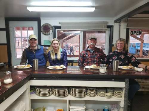 Four people sitting at a counter in a diner, enjoying meals with plates of food in front of them.
