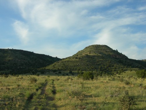A scenic view of rolling hills under a blue sky, with a dirt path leading through a grassy landscape.