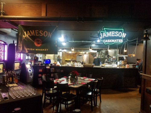 A cozy bar area with Jameson whiskey signage, a dining table set, and a visible kitchen in the background.