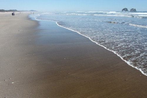 A serene beach scene with gentle waves lapping at the shore and distant figures walking along the sandy coastline.