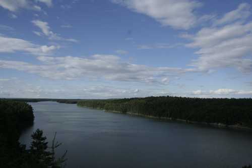 A serene river flows through a lush green landscape under a partly cloudy sky.