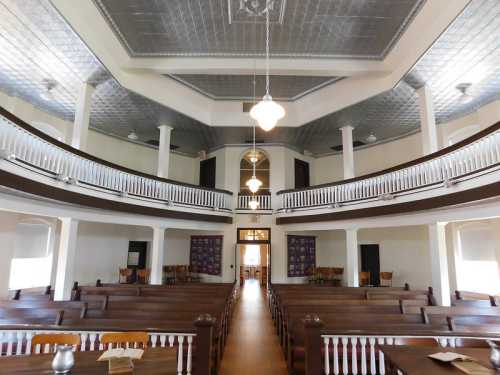 Interior of a historic church featuring wooden pews, a high ceiling, and balcony seating. Natural light illuminates the space.