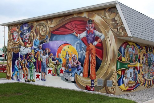 Colorful mural depicting clowns and circus performers in a vibrant, whimsical scene on the side of a building.