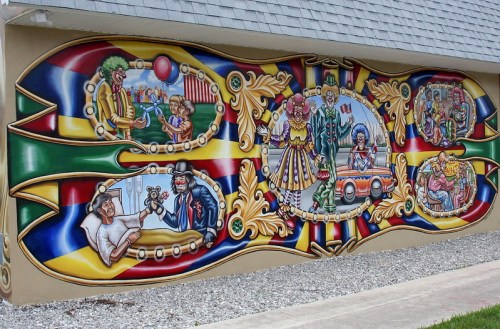 Colorful mural depicting circus scenes with clowns, performers, and playful characters on a building wall.