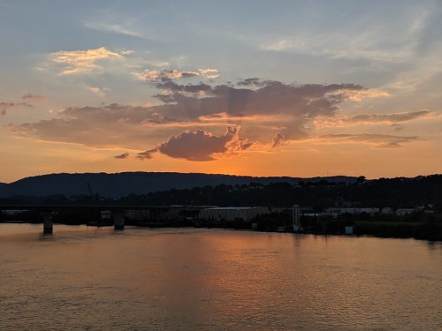 Sunset over a river, with vibrant orange and purple clouds reflecting on the water and hills in the background.