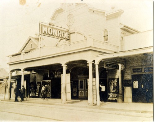 Historic photo of the Monroe theater, featuring vintage signage and people outside the entrance.