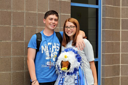 Two smiling students pose together, one wearing a blue shirt and the other in a white shirt, with a decorated eagle mascot.