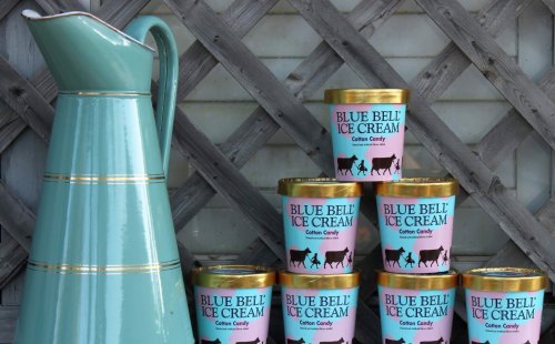 A vintage teal pitcher next to stacked containers of Blue Bell cotton candy ice cream against a lattice background.