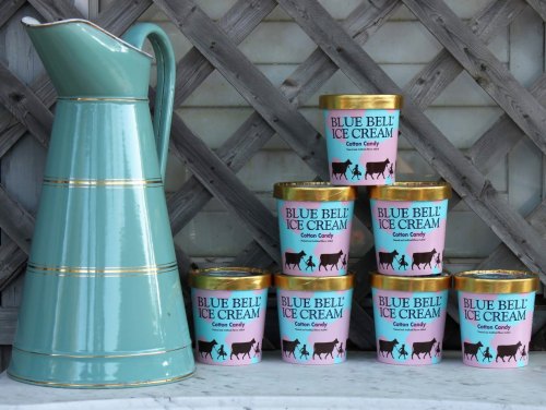 A vintage pitcher next to stacked containers of Blue Bell Cotton Candy ice cream against a wooden backdrop.