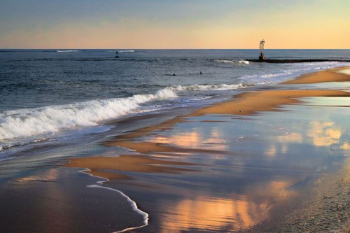 A serene beach scene at sunset, with gentle waves, golden sand, and reflections in the water.