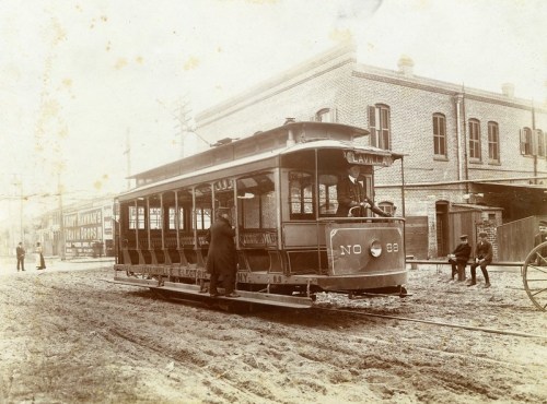 A vintage streetcar labeled "No. 88" on a dirt road, with people nearby and buildings in the background.