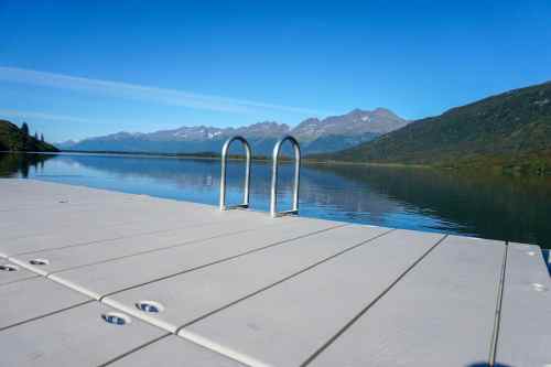 A serene lake view from a wooden dock, with mountains in the background under a clear blue sky.