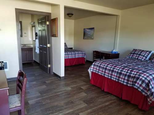 A spacious hotel room with two beds, a desk, and a bathroom area, featuring wooden floors and plaid bedding.