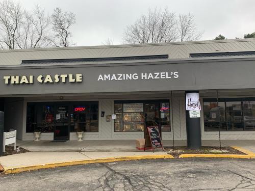 Exterior of a shopping plaza featuring "Thai Castle" and "Amazing Hazel's" signs, with an open sign in the window.