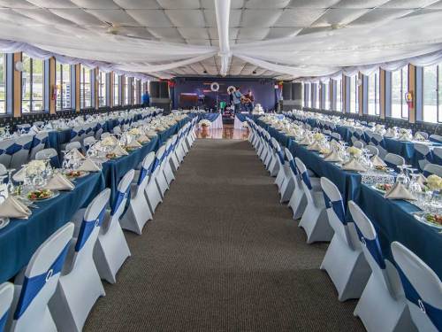 A spacious banquet hall set for an event, featuring long tables with blue tablecloths and elegant place settings.