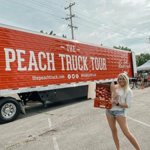 A woman holds a basket of peaches in front of a large truck labeled "The Peach Truck Tour."