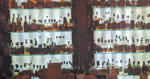 A well-stocked bar with shelves of various whiskey bottles illuminated by soft lighting.