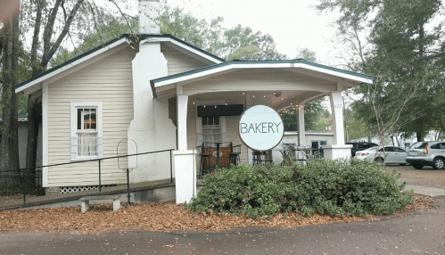 A charming bakery with a porch, surrounded by trees and autumn leaves, featuring a large sign that says "BAKERY."