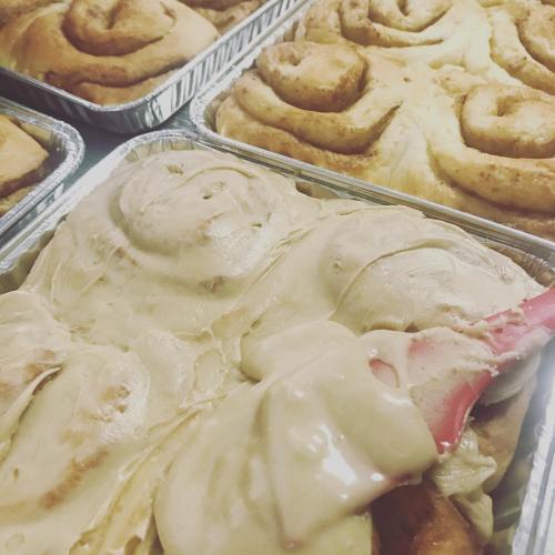 Freshly baked cinnamon rolls topped with creamy frosting in aluminum trays.