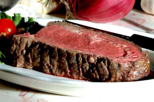 A close-up of a perfectly cooked slice of beef on a plate, garnished with greens and cherry tomatoes.