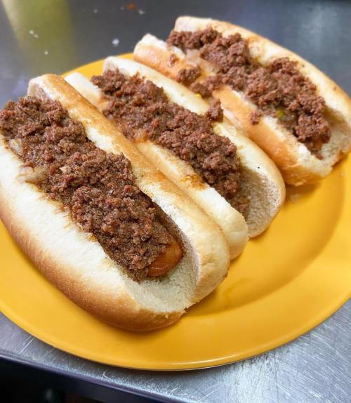Three hot dogs topped with a generous layer of meat chili, served on a yellow plate.
