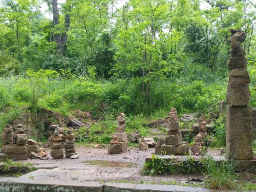 A serene forest scene featuring stacked stone formations surrounded by lush greenery and trees.