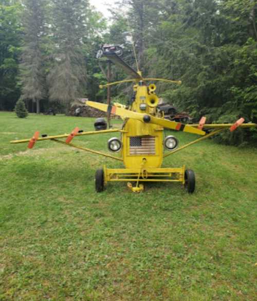 A yellow agricultural helicopter parked on grass, surrounded by trees, with various attachments and lights.