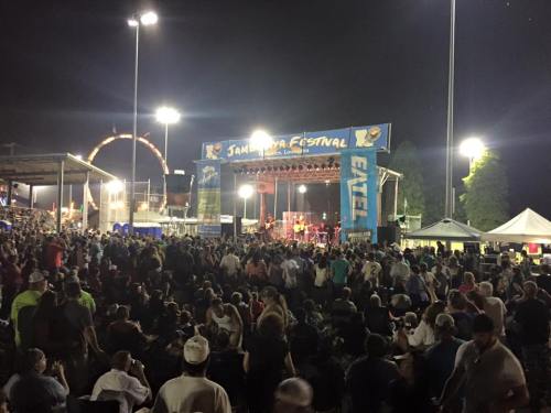 A large crowd enjoys a nighttime concert at the Jambalaya Festival, with bright lights and a festive atmosphere.