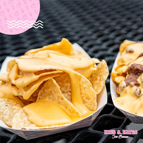 A close-up of nachos topped with melted cheese, served in a paper tray on a black surface.