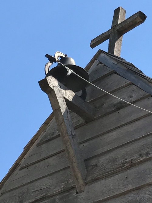 A wooden church roof with a bell and two crosses against a clear blue sky.