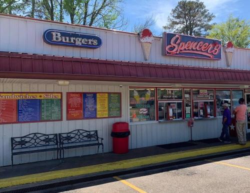 A colorful fast-food stand with a menu, serving burgers and ice cream, and a bench outside. People are ordering at the window.