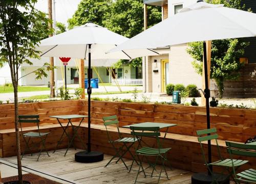 Outdoor seating area with green tables and chairs, shaded by white umbrellas, surrounded by wooden planters.