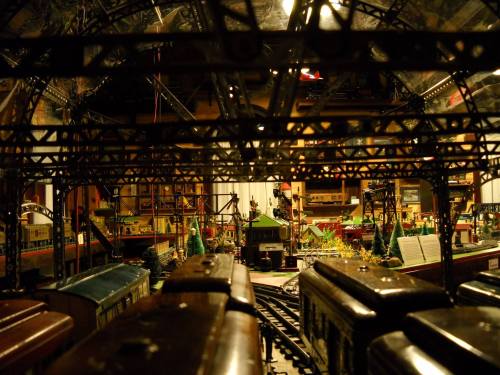 A detailed model train setup featuring tracks, buildings, and miniature scenery under a structured overhead framework.